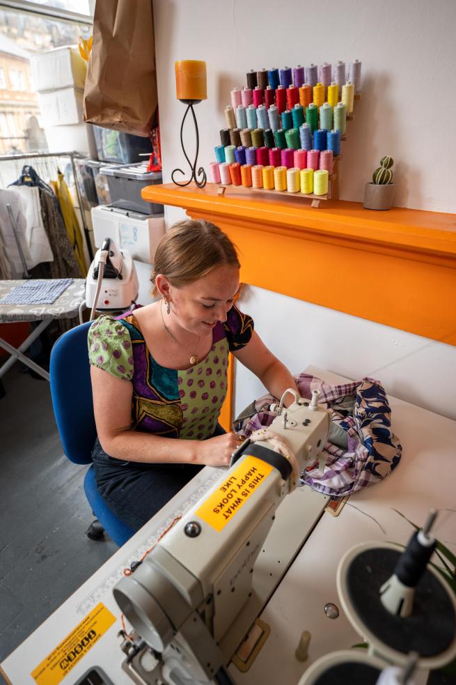 Woman at a sewing machine, making clothes, in a workshop.