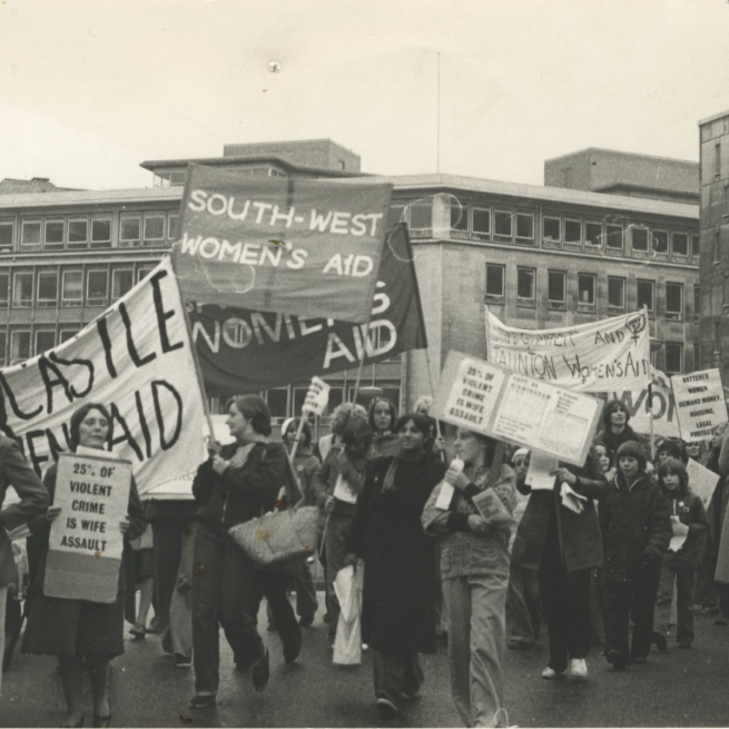 A black and white photo of women and children marching down the street with Women's Aid banners