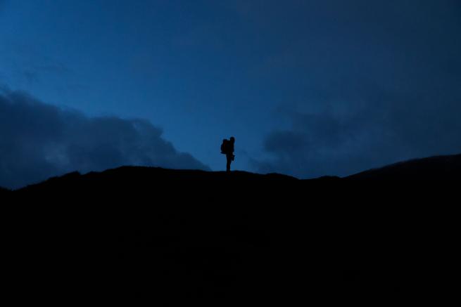 Silhouette of a man stood on top of a mountain at night.