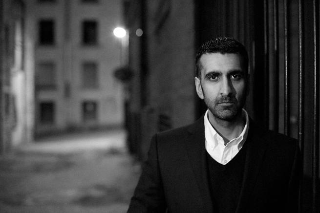 Black an white photo of the author AA Dhand standing in a street with street light in distance behind him