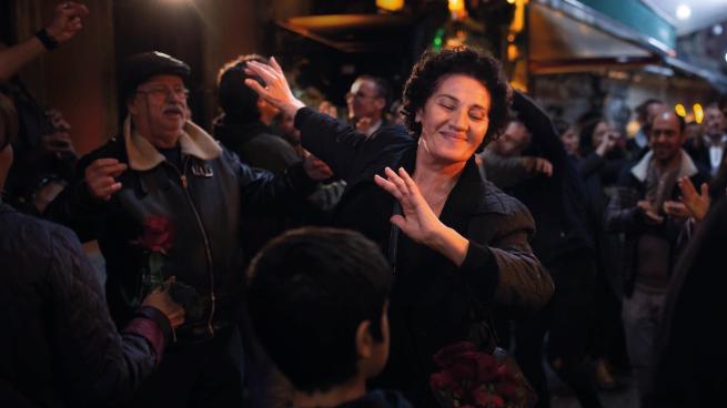 Middle-aged woman dancing at night in crowd outside.