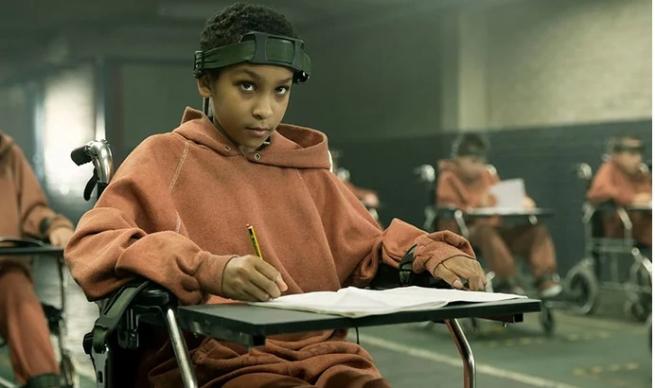 Black girl sat in prison-like school setting with a metal bar around her head.