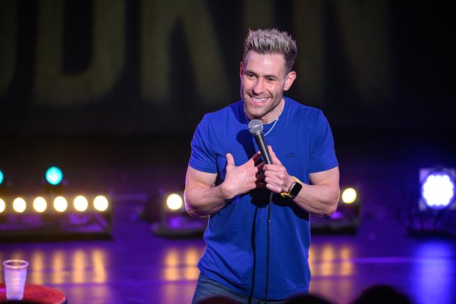 Simon Brodkin on stage in a blue t-shirt