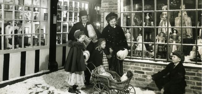 Black and white picture of a family dressed in period costume on Abbey House Museum Street, which has a festive feel with fake snow on the paved floor.