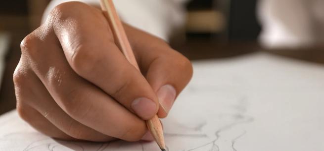 A picture of a hand with a pencil in it, writing on a piece of paper 