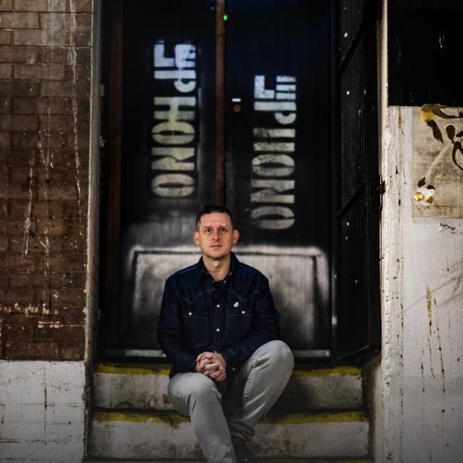 A man sits on steps outside a disused club entrance - Le Phono