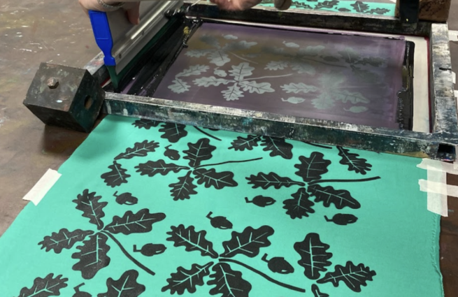A pattern of leaves being screen printed in black on green fabric