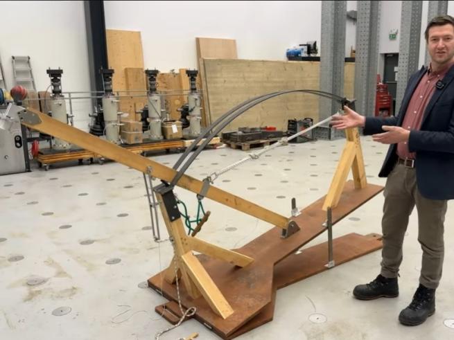 A photo of the Venn Bowling Machine, built from wood, with Thomas Glenday from University of Cambridge stood next to it