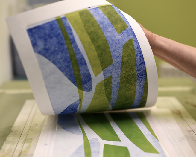 An abstract print on blues and greens being revealed on paper