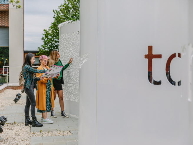 Three people looking at a map stood by a white metal sculpture with patterns and letters cut from it.
