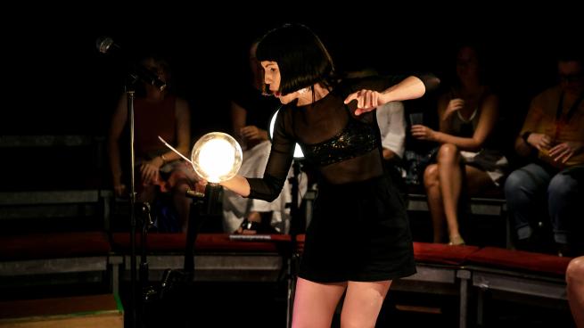 A woman performing spoken word in front of a large orb light