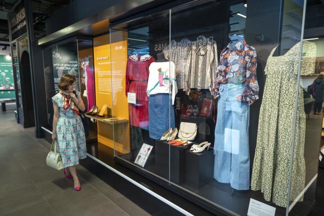 A woman walks through the M&S Archive exhibition, looking into a display case with garments on mannequins