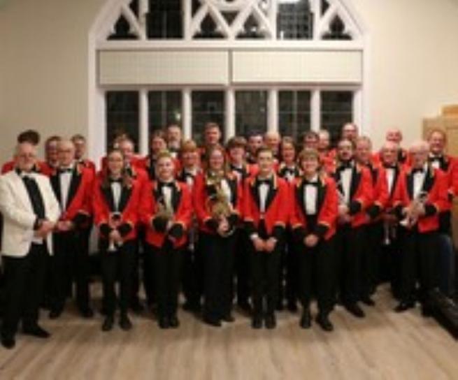 Very smart looking Brass Band dressed in red jackets with black lapels holding various brass instruments. They look like a very tidy bunch of people