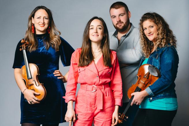 Fantastic looking band with three female and one male member they are smiling at the camera and holding fiddles and whistles