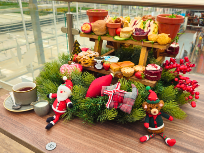 Festive afternoon tea at The Arium. A selection of sweet and savoury festive snacks sit on a wooden stand, surrounded by Christmas decorations.
