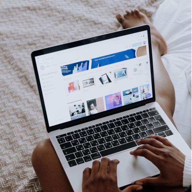 A photograph taken over someone's shoulder showing them using Canva on a laptop