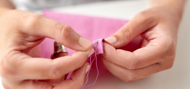 Picture pf a pair of hands stitching with a needle and pink cloth