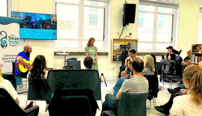Room with people sat watching people playing guitar and singing