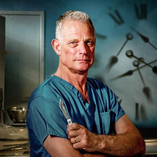 Dr Richard Shepherd stands with arms crossed, holding a scalpel and wearing blue scrubs in a clinical setting. A shadowy clock is visible in the background.