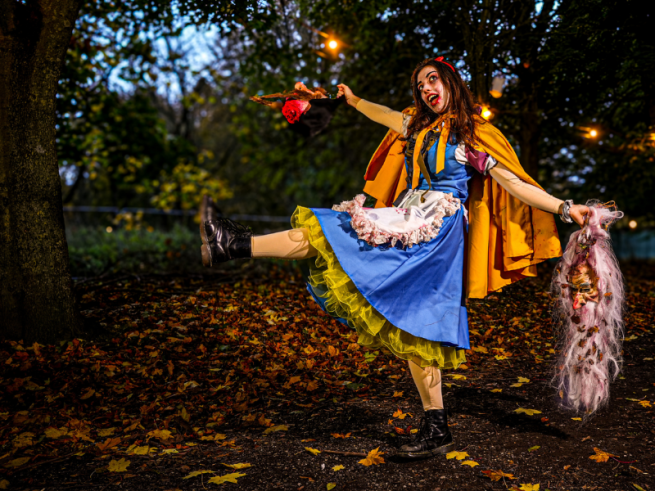 lady dressed as a dark version of Snow White, holding halloween props standing in a darkened woods