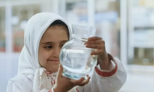 A young girl exams a glass container.
