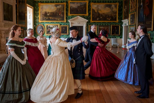 There are 4 couples in Victorian dancing the waltz cotillion. Two couples in hold are dancing the waltz step. The other 2 couples are at the side of the square waiting their turn.