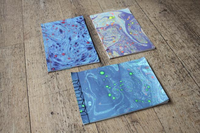 Image shows three hand stitched and marbled books on a wooden background.
