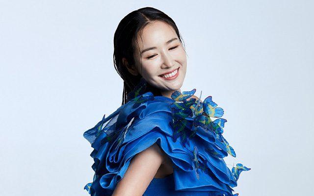 A woman smiling in a blue dress adorned with large decorative butterflies