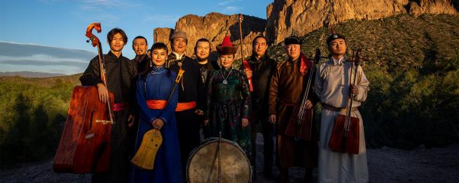 A group shot of the nine members of Anda Union standing with their instruments in an outdoor setting.