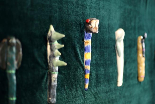 Collection of ceramic wands displayed on top of green velvet fabric. Each wand is different with the centre having a snakes head and striped yellow and blue handle.