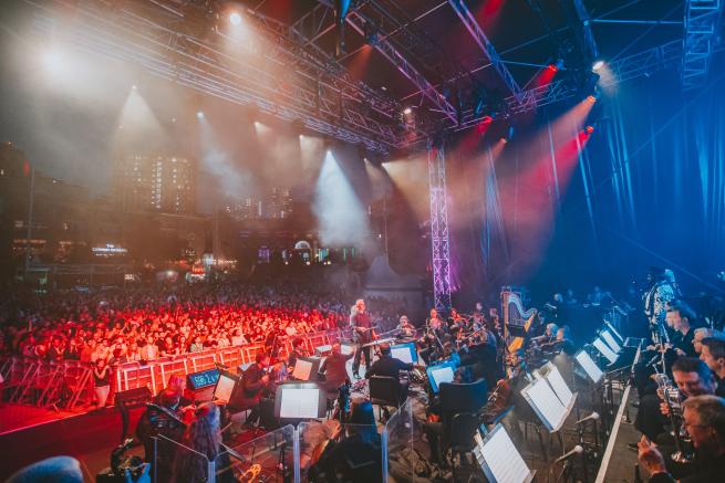 The Orchestra Of Opera North performing on stage at Millennium Square in front of a crowd of people