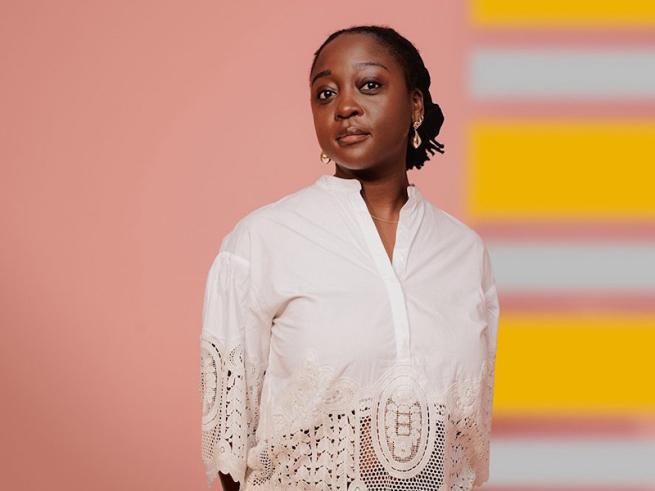 A woman wearing a white shirt standing in front of a colourful background.