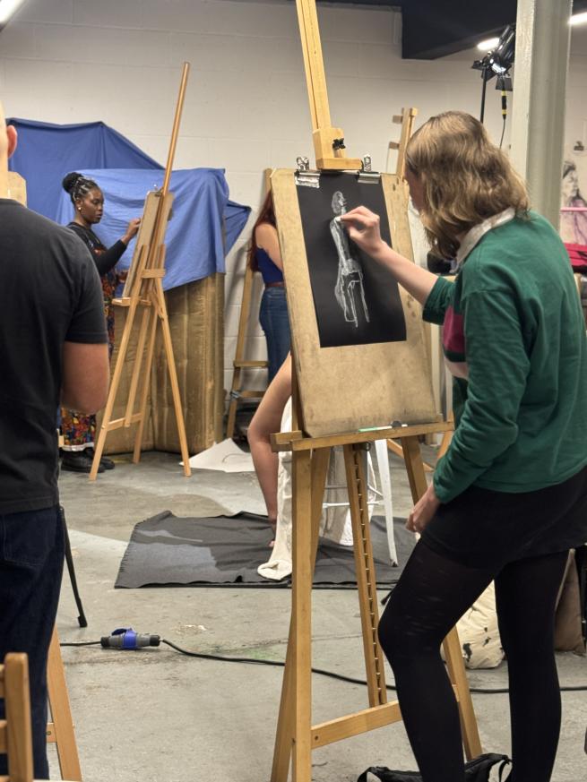 A life drawing class showing artists standing at easels drawing with white chalk on black paper