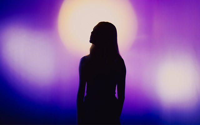 A silhouette of a woman standing in front of blurred purple lights