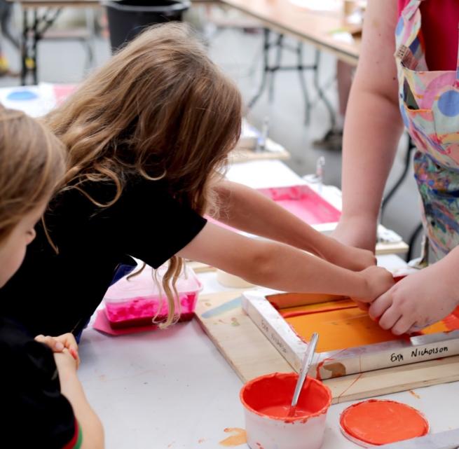 A child creates a screenprint with orange paint
