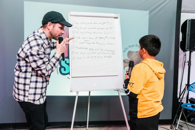 A rapper teaching a younger rapper using a flipchart