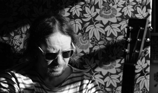 A man, a guitar, a striped shirt, a floral wallpaper background and shades