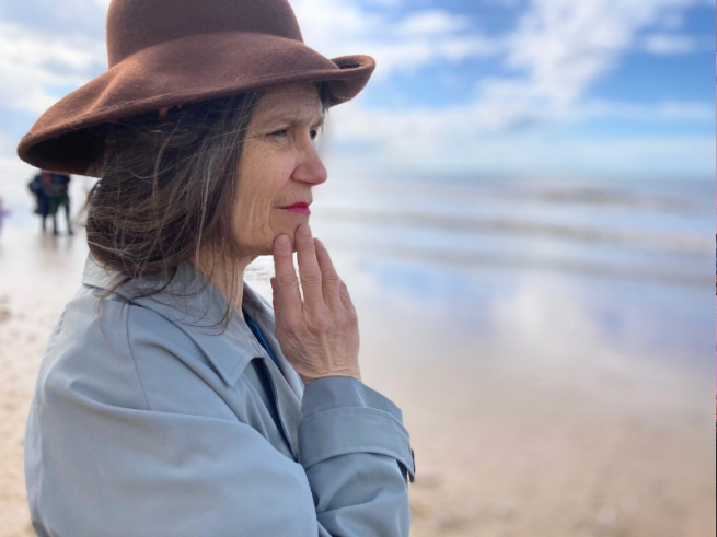 A woman stood on a beach wearing a hat, looking into the horizon.