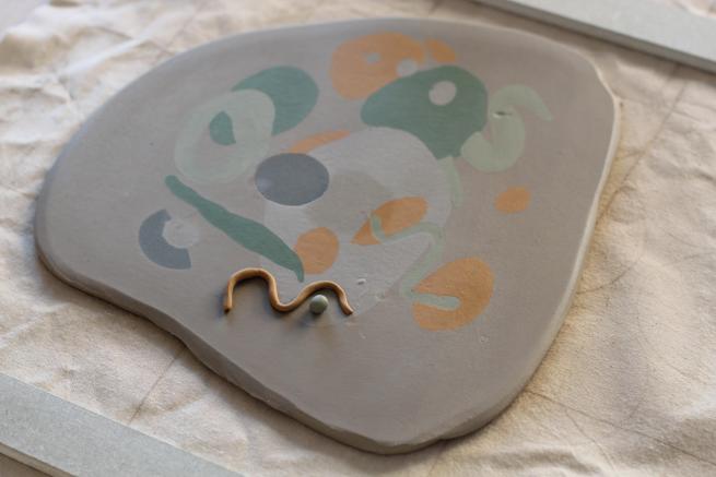 Image shows a slab of rolled out white clay with coloured clay patterns imprinted into it. 