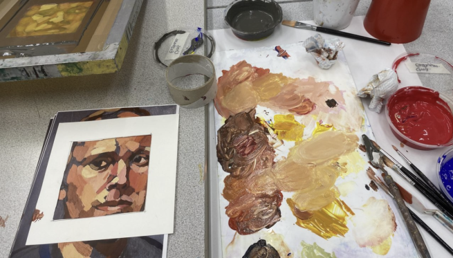 An assortment of paints and brushes next to a stylised portrait of a man