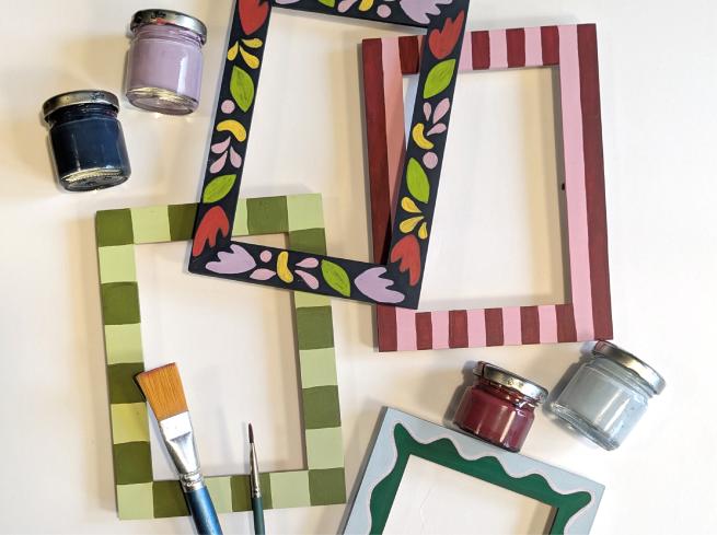 Hand painted photo frames next to pots of paint and brushes