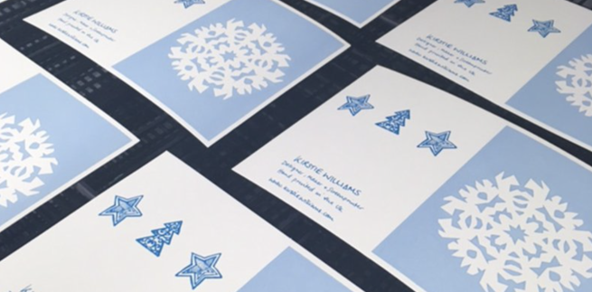 Screen printed Christmas cards with a snowflake design in blue drying on a drying rack