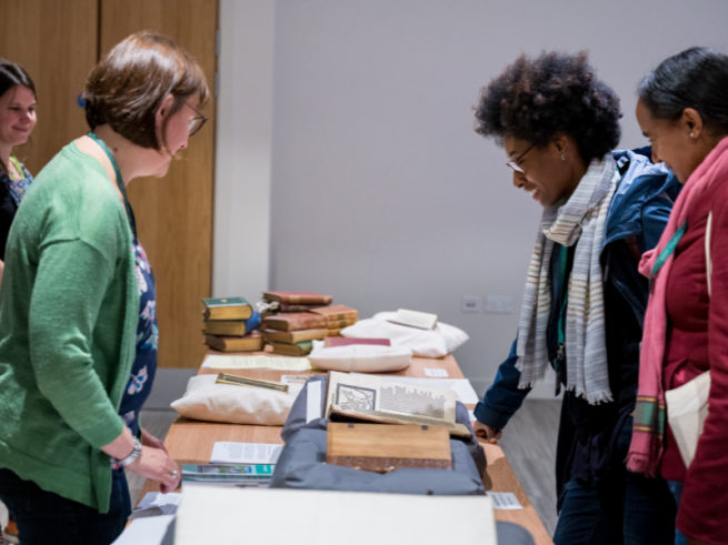 People stood either side of a table filled with open books resting on cushions.