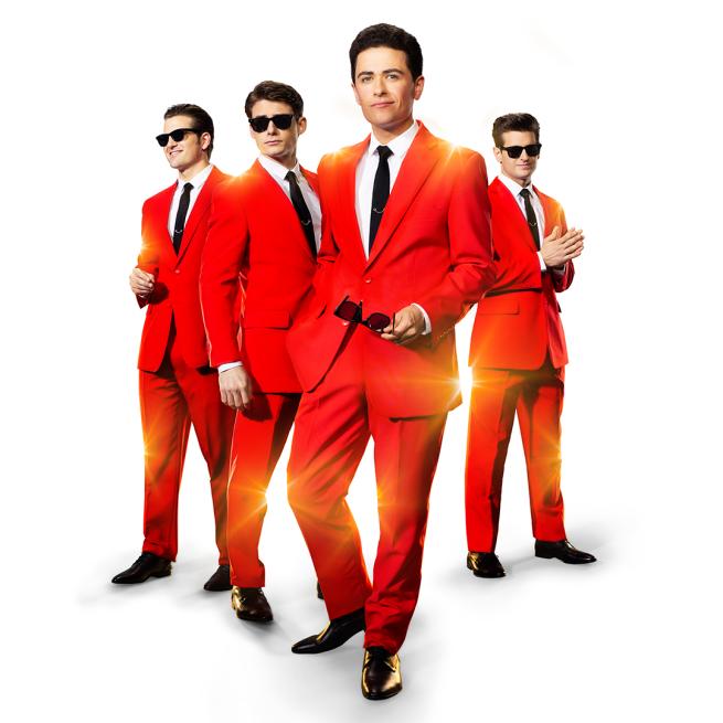 Four men in matching sunglasses and red suits suavely stand together and shimmer in golden light.