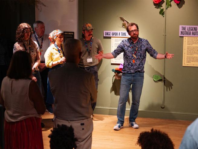 Museum curator leading a talk in an exhibition space, with people looking at him and listening.