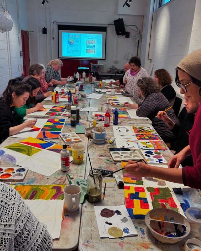 A group of people sitting at a table painting abstract shapes with primary colours.