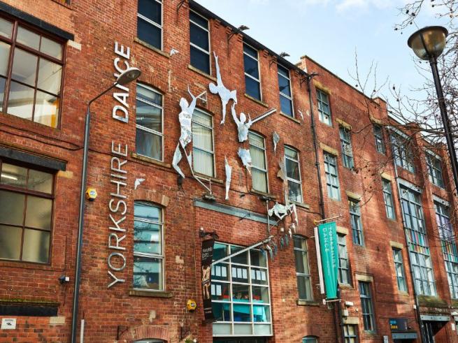 An image of a large red brick building with the words Yorkshire Dance in silver letters