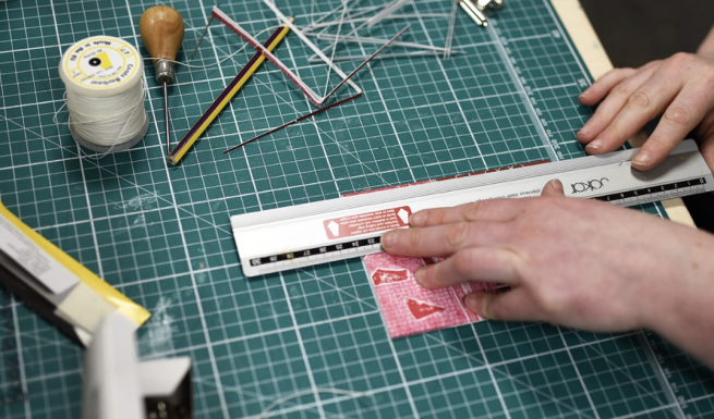 A hand bound book being made, with tools such as a metal ruler, thread and an awl