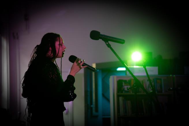 Performer sings in a darkened room with green light in back ground