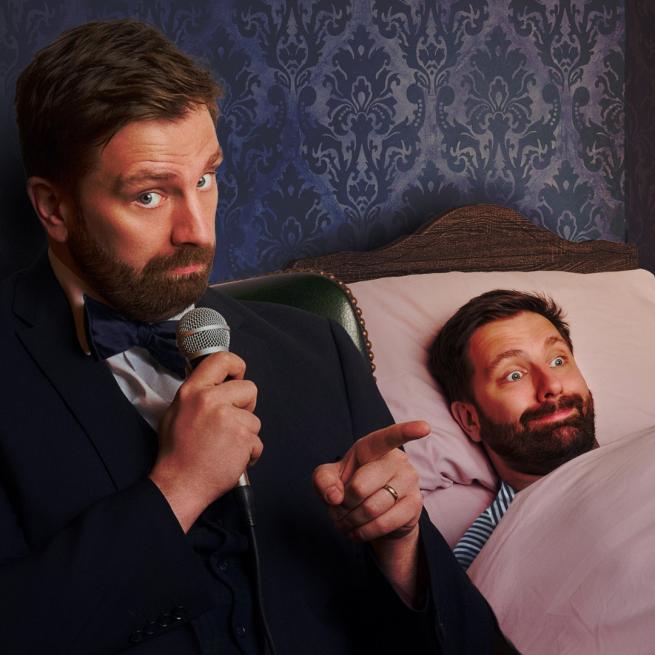 Pierre Novellie sits beside a bed, holding a microphone. In the bed, a second Pierre Novellie is tucked in beneath a pink blanket with a comical smile.